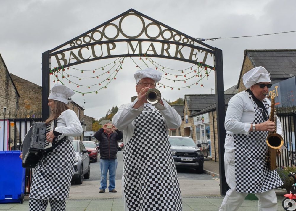 Men dressed as chefs playing instruments at the entrance to Bacup Market