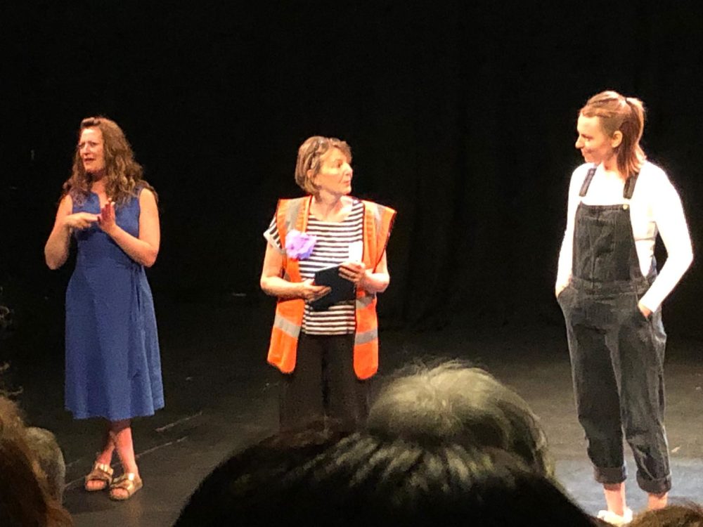 Three women stand on stage